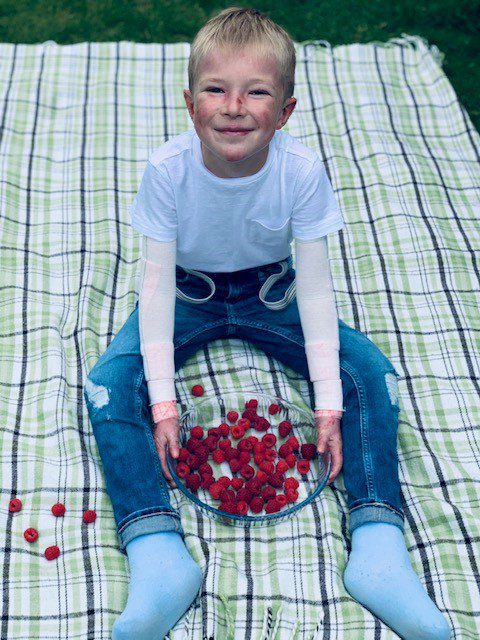 Gabrielius on a picnic mat holding a bowl of raspberries