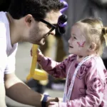 Small child with EB holding a balloon animal and smiling up at father