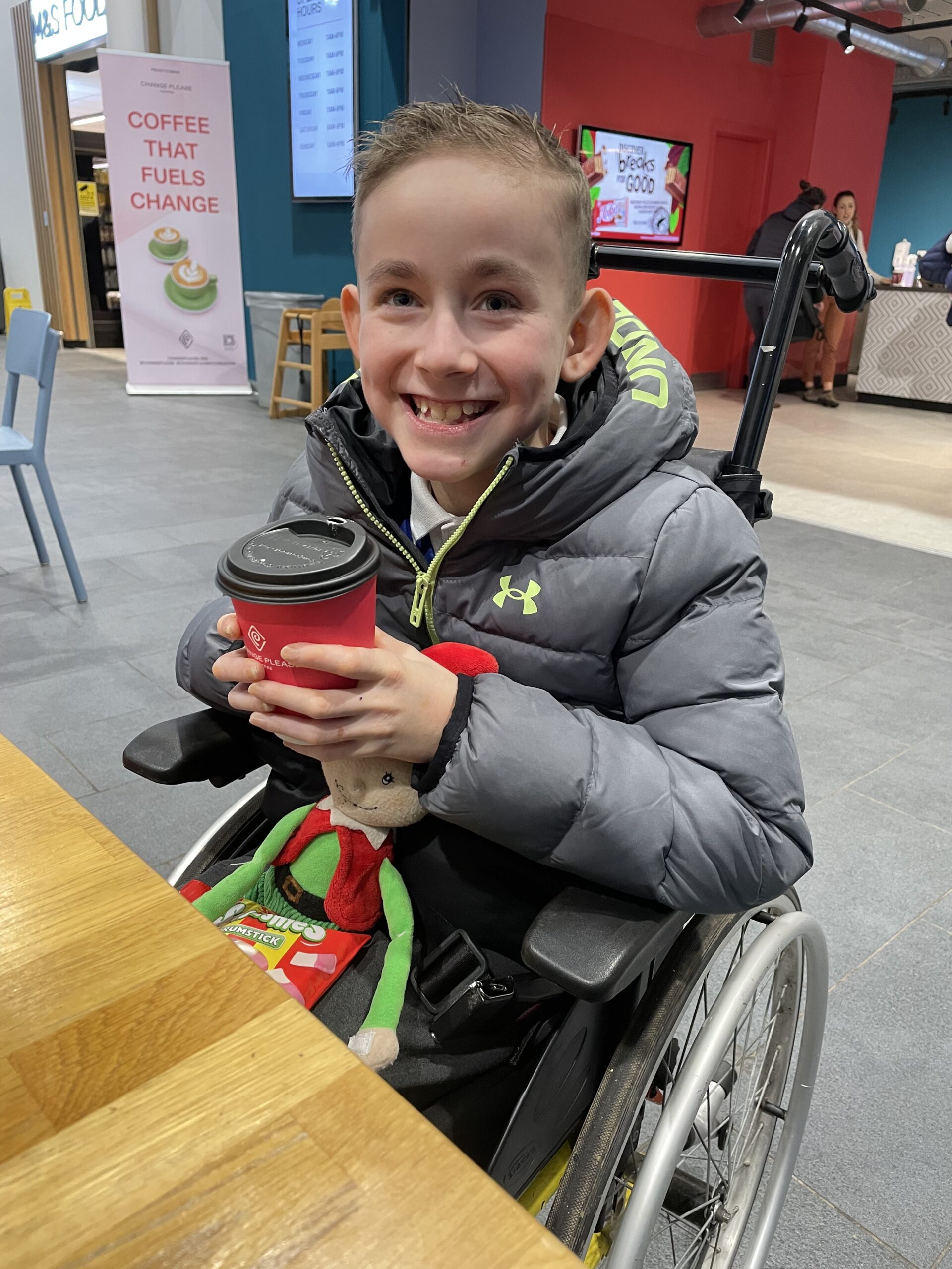 Photo of a smiling young boy with Junctional EB, sitting at a table in a wheelchair.